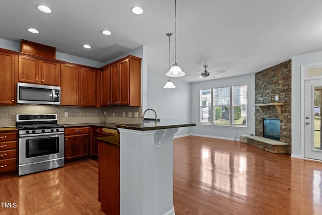 kitchen with tasteful backsplash, appliances with stainless steel finishes, pendant lighting, light hardwood / wood-style floors, and kitchen peninsula