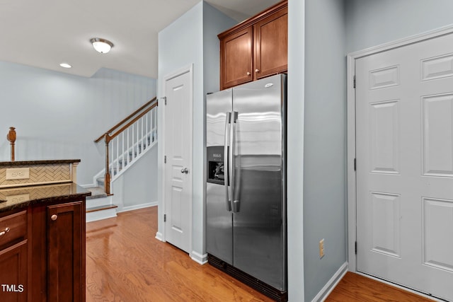 kitchen featuring dark stone countertops, light wood-type flooring, and stainless steel refrigerator with ice dispenser