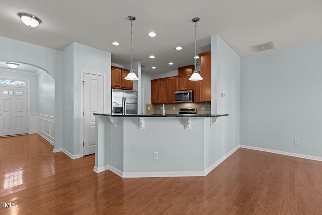 kitchen with appliances with stainless steel finishes, decorative light fixtures, hardwood / wood-style floors, a breakfast bar area, and kitchen peninsula