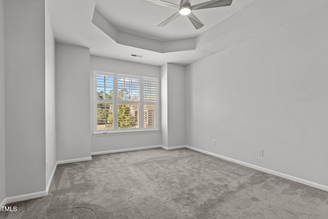 spare room featuring light colored carpet, ceiling fan, and a raised ceiling