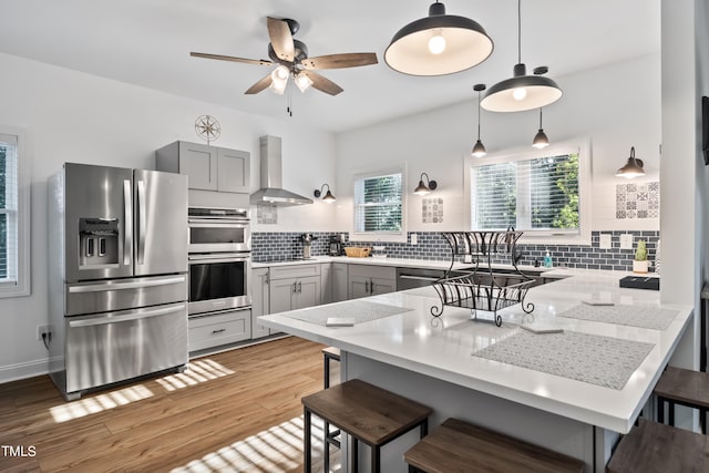 kitchen with stainless steel appliances, kitchen peninsula, wall chimney range hood, and gray cabinetry