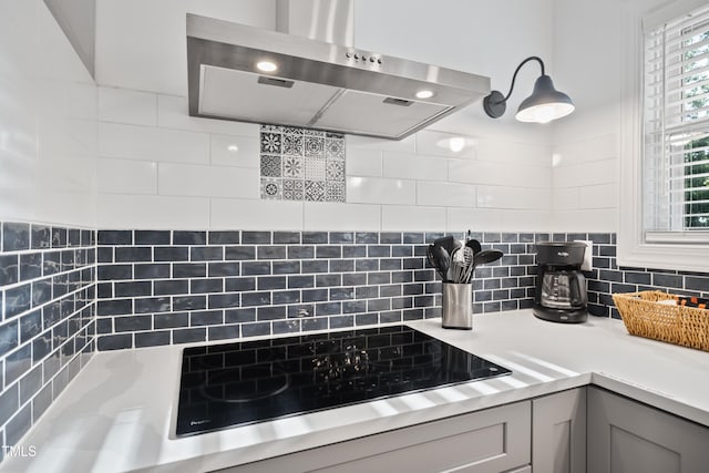 interior space featuring range hood, decorative backsplash, cooktop, and gray cabinets