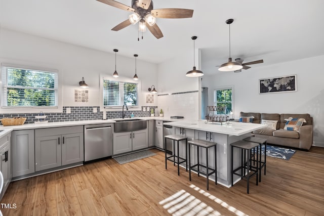 kitchen with sink, kitchen peninsula, a kitchen breakfast bar, decorative light fixtures, and stainless steel dishwasher