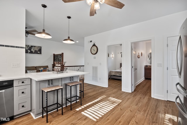 kitchen featuring ceiling fan, hanging light fixtures, kitchen peninsula, a breakfast bar, and light wood-type flooring