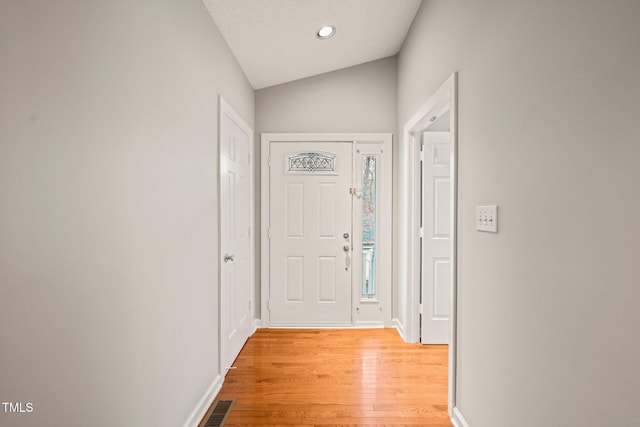 doorway to outside with a textured ceiling, vaulted ceiling, and light wood-type flooring