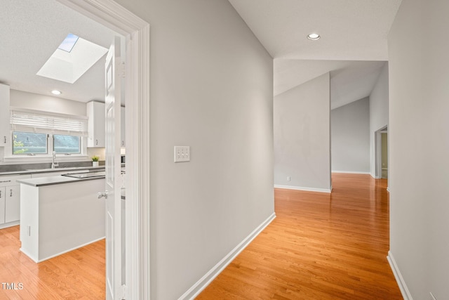 hall with lofted ceiling with skylight, sink, and light hardwood / wood-style flooring