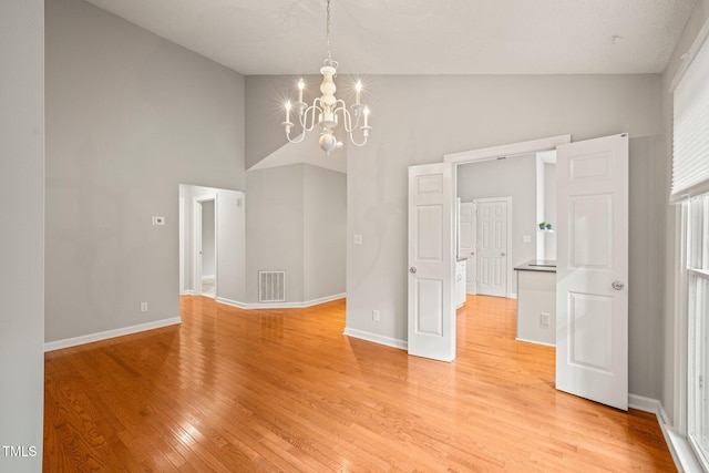 unfurnished room with an inviting chandelier, a textured ceiling, high vaulted ceiling, and light hardwood / wood-style flooring