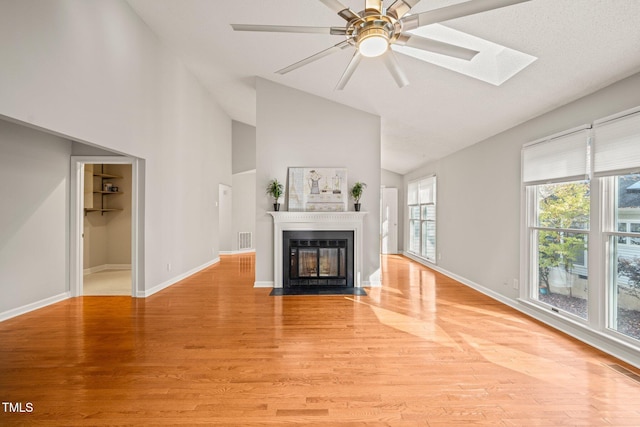 unfurnished living room with ceiling fan, light wood-type flooring, high vaulted ceiling, and a skylight