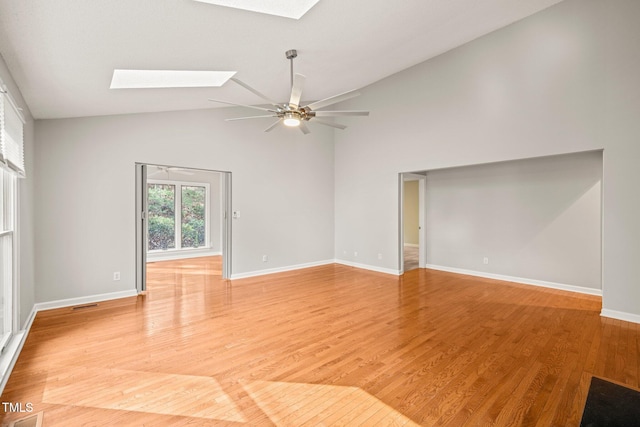 unfurnished room with a skylight, ceiling fan, light hardwood / wood-style flooring, and high vaulted ceiling