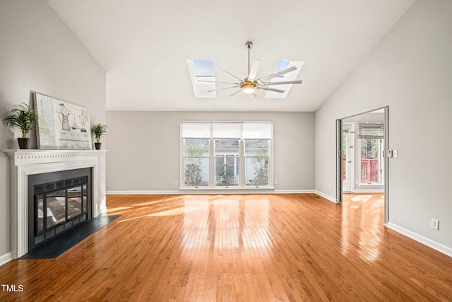 unfurnished living room featuring ceiling fan, light wood-type flooring, high vaulted ceiling, and a skylight