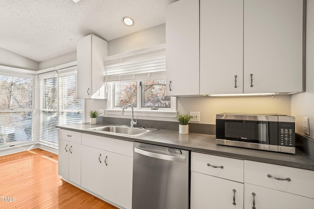 kitchen with white cabinets, sink, light wood-type flooring, a textured ceiling, and appliances with stainless steel finishes