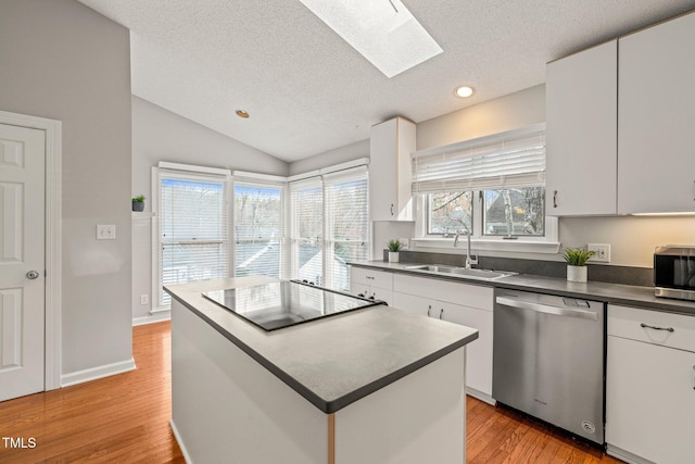 kitchen featuring white cabinets, appliances with stainless steel finishes, vaulted ceiling with skylight, and sink