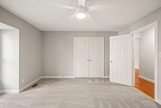 unfurnished bedroom featuring light carpet, a textured ceiling, a closet, and ceiling fan