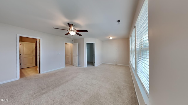 unfurnished bedroom with a walk in closet, ceiling fan, and light colored carpet