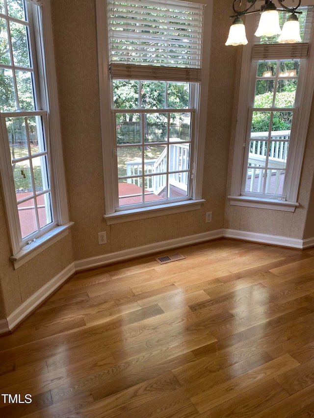 unfurnished dining area with hardwood / wood-style floors, a wealth of natural light, and a notable chandelier