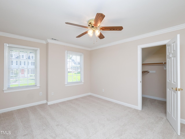 unfurnished bedroom with light colored carpet, a spacious closet, ceiling fan, and ornamental molding