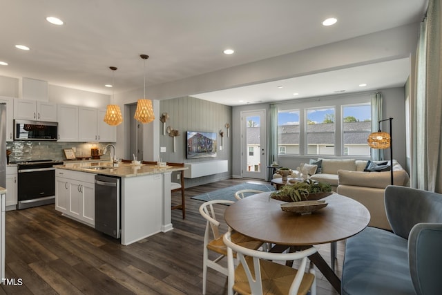 kitchen featuring an island with sink, white cabinets, stainless steel appliances, decorative light fixtures, and light stone countertops