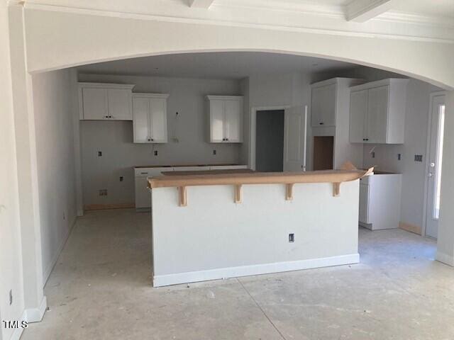 kitchen with beamed ceiling, white cabinetry, and a breakfast bar area