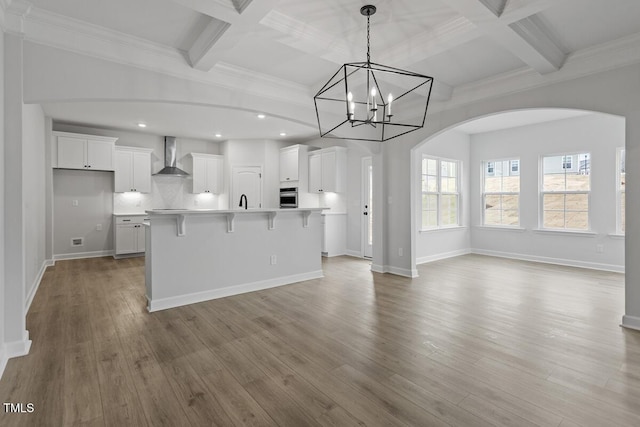 kitchen with a kitchen bar, decorative light fixtures, wall chimney exhaust hood, white cabinets, and a kitchen island with sink