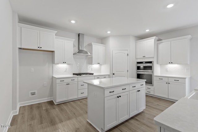 kitchen with light hardwood / wood-style flooring, double oven, wall chimney exhaust hood, a center island, and white cabinetry