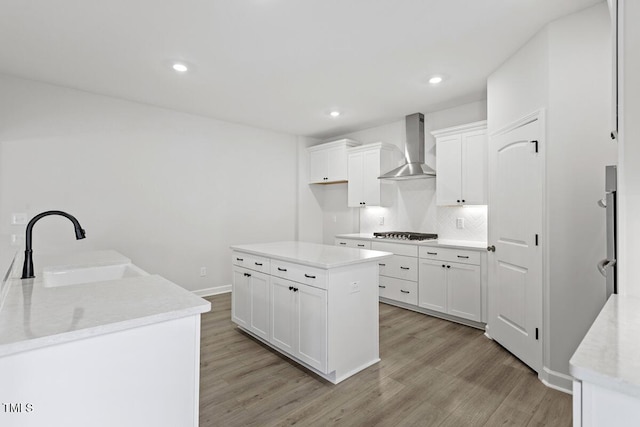 kitchen with a kitchen island, sink, white cabinetry, and wall chimney range hood