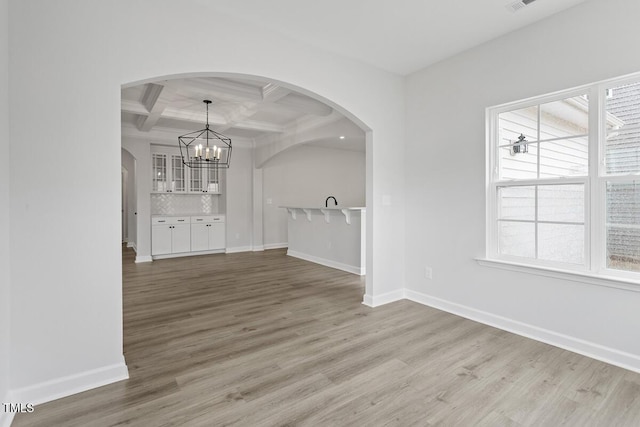 unfurnished dining area featuring coffered ceiling, an inviting chandelier, wood-type flooring, and beamed ceiling