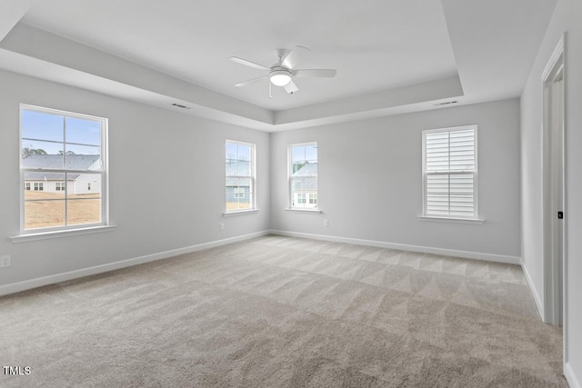 empty room featuring a tray ceiling, ceiling fan, and light carpet