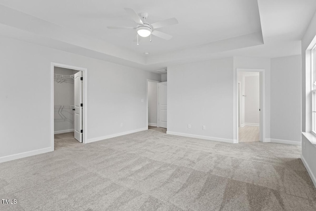 unfurnished bedroom featuring a spacious closet, a closet, ceiling fan, a raised ceiling, and light carpet