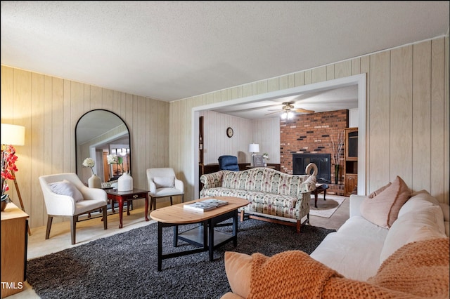 living room with wood walls, carpet flooring, a fireplace, a textured ceiling, and ceiling fan