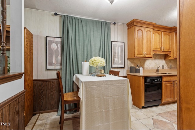 kitchen with black dishwasher, backsplash, a kitchen breakfast bar, a textured ceiling, and wood walls