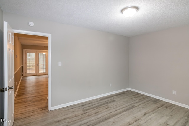 empty room featuring light hardwood / wood-style flooring, a textured ceiling, and french doors