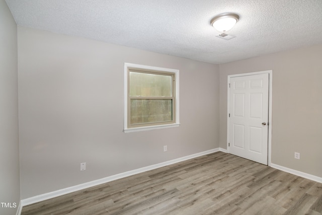 spare room with light wood-type flooring and a textured ceiling