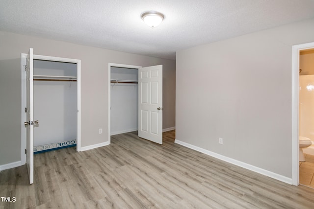 unfurnished bedroom featuring two closets, a textured ceiling, light hardwood / wood-style flooring, and connected bathroom