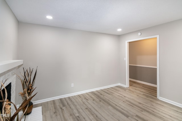 unfurnished living room featuring a brick fireplace, light hardwood / wood-style floors, and a textured ceiling