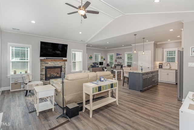 living room with lofted ceiling, ceiling fan, a stone fireplace, dark hardwood / wood-style floors, and crown molding