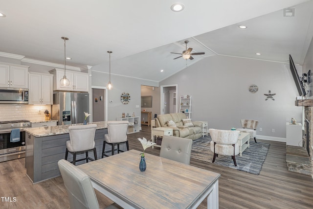 dining room with ceiling fan, a fireplace, vaulted ceiling, and dark hardwood / wood-style flooring