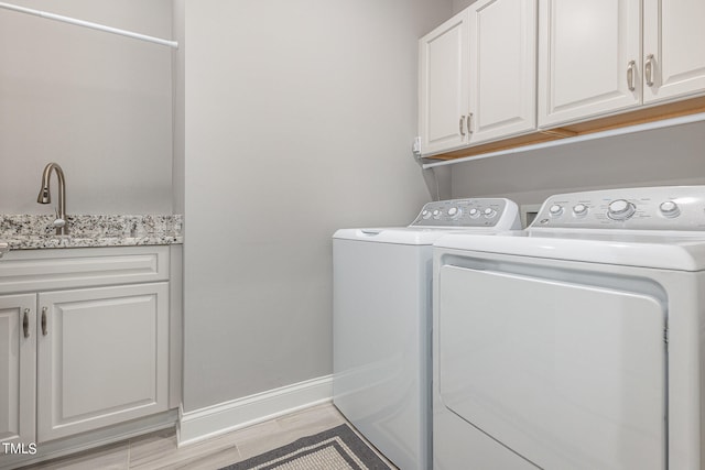 laundry area with sink, washer and clothes dryer, light hardwood / wood-style flooring, and cabinets