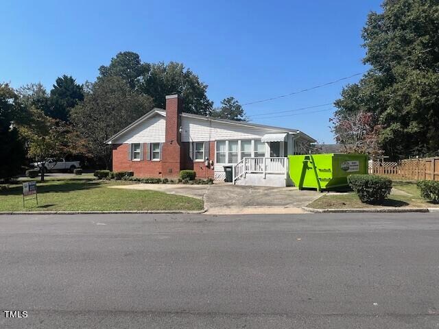 view of front facade with concrete driveway, fence, a chimney, and a front lawn