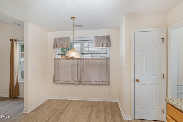 unfurnished dining area with light hardwood / wood-style floors and a textured ceiling