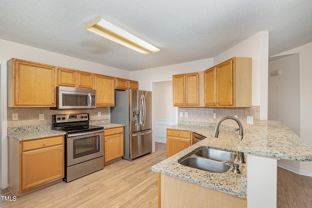 kitchen featuring light stone countertops, sink, light wood-type flooring, kitchen peninsula, and stainless steel appliances