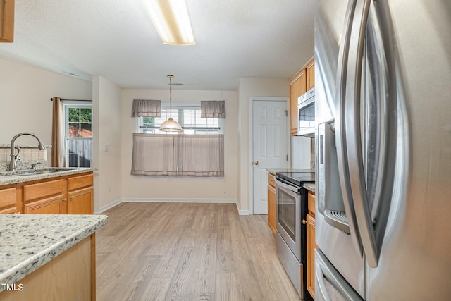 kitchen featuring sink, a textured ceiling, stainless steel appliances, decorative light fixtures, and light hardwood / wood-style flooring