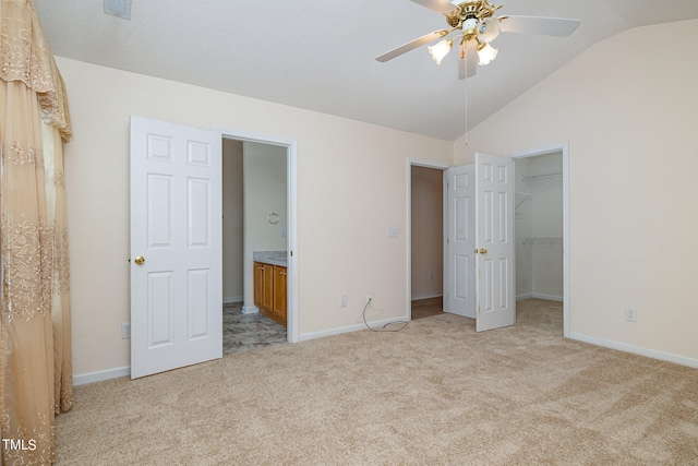 unfurnished bedroom featuring connected bathroom, a walk in closet, vaulted ceiling, light colored carpet, and ceiling fan