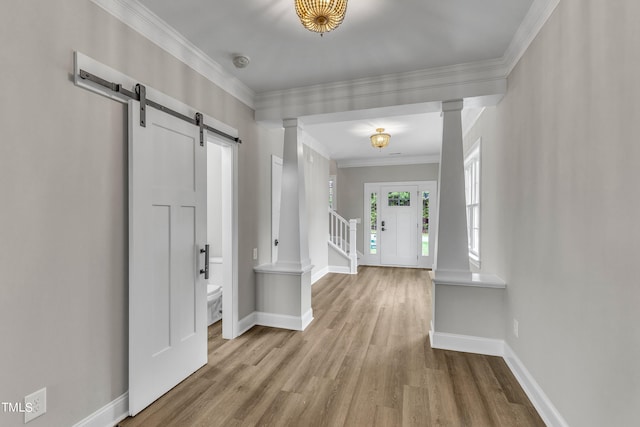 foyer featuring a barn door, decorative columns, light hardwood / wood-style floors, and ornamental molding