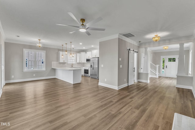 unfurnished living room with a barn door, wood-type flooring, ornamental molding, and ceiling fan