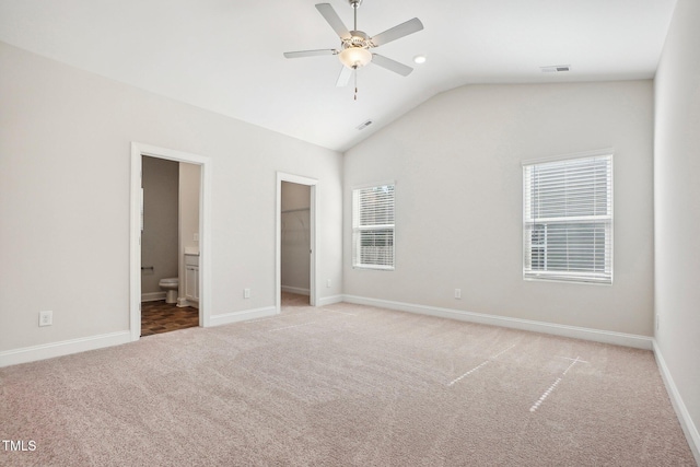 unfurnished bedroom featuring visible vents, connected bathroom, light colored carpet, a spacious closet, and vaulted ceiling