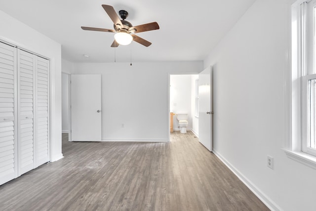 unfurnished bedroom featuring wood-type flooring, ceiling fan, ensuite bathroom, and a closet