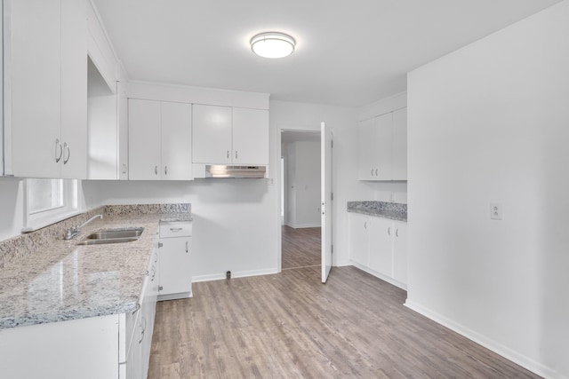 kitchen featuring light wood-type flooring, light stone countertops, white cabinetry, and sink