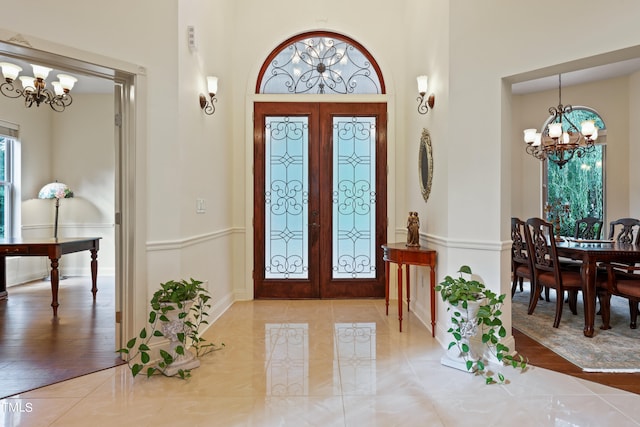 entryway with french doors, a notable chandelier, a towering ceiling, and hardwood / wood-style flooring