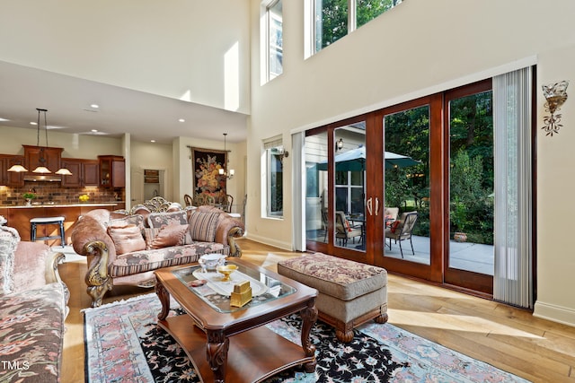 living room featuring a high ceiling, a chandelier, light hardwood / wood-style floors, and a healthy amount of sunlight