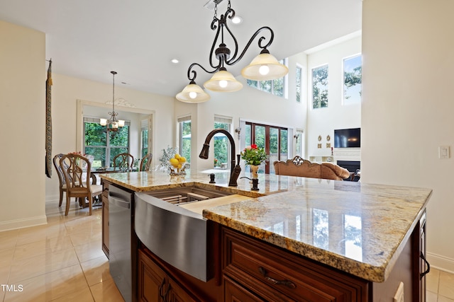 kitchen with pendant lighting, a chandelier, an island with sink, light stone countertops, and stainless steel dishwasher